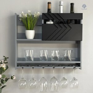 May include: A gray wall mounted wine rack with two shelves and a black wine bottle holder. The rack has six glass holders underneath. There are three bottles of wine and a plant on the top shelf.