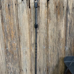May include: A black wrought iron fireplace tool set, including a poker and a hanging bracket. The poker has a twisted handle and a hook at the end. The bracket has hooks for hanging the tools. The set is mounted on a wooden wall.