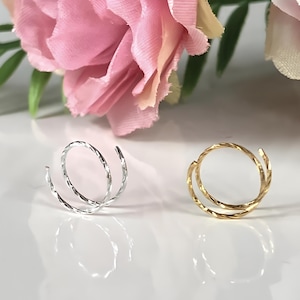 May include: Two nose rings, one silver and one gold, are shown on a white surface. Both rings are twisted and have a shiny finish.