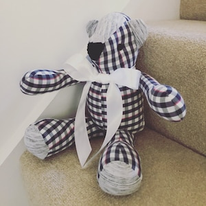 May include: A plaid teddy bear with a white bow. The bear is sitting on a carpeted staircase.