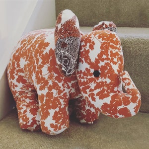 May include: A white and orange elephant doorstop with a leafy pattern. The elephant has a long trunk and large ears.