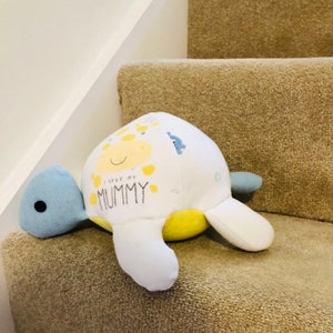 May include: A white and yellow stuffed turtle toy with a blue head and feet. The turtle has a smiling face and the words "I love my MUMMY" printed on its shell.