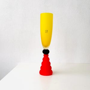 May include: A tall, colorful glass with a yellow top and a red, cone-shaped base. The glass has a black band between the yellow top and red base. The text "LLD" is printed on the yellow glass.