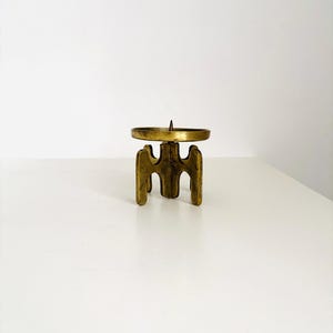 Könnte beinhalten: Ein Vintage-Kerzenhalter aus Messing mit einem einzigartigen, skulpturalen Design. Der Kerzenhalter hat eine runde Plattform für die Kerze und einen dreibeinigen Sockel. Das Messing hat eine warme, gealterte Patina, die seinen Vintage-Reiz unterstreicht. Ein dekoratives Element.