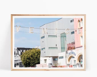 May include: A framed photograph of a street scene in Venice, California. The photo features a building with a sign that reads "Venice Beach Park" and a string of lights spelling out "VENICE".