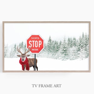 Puede incluir: Una se&ntilde;al de stop roja con las palabras "Santa Stop Here" en texto blanco, con un ciervo con una bufanda roja de pie frente a ella en un entorno de bosque nevado.