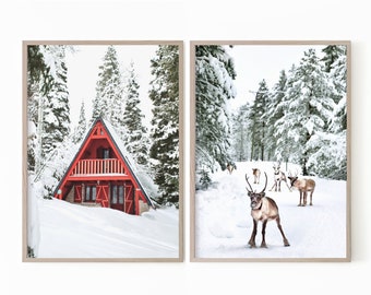 May include: A set of two framed winter landscape prints. The first print shows a red cabin in a snowy forest. The second print shows a group of reindeer walking through a snowy forest.