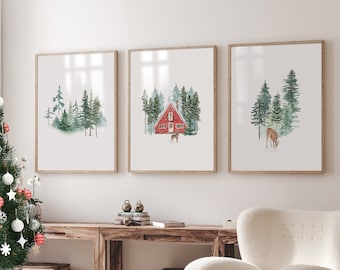May include: Three watercolor paintings in wooden frames depicting a winter forest scene. The center painting shows a red cabin with a snowy roof and trees in the background. The left and right paintings show a deer in the forest.