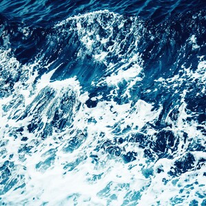 May include: Close-up of white foam waves crashing on a deep blue ocean surface.