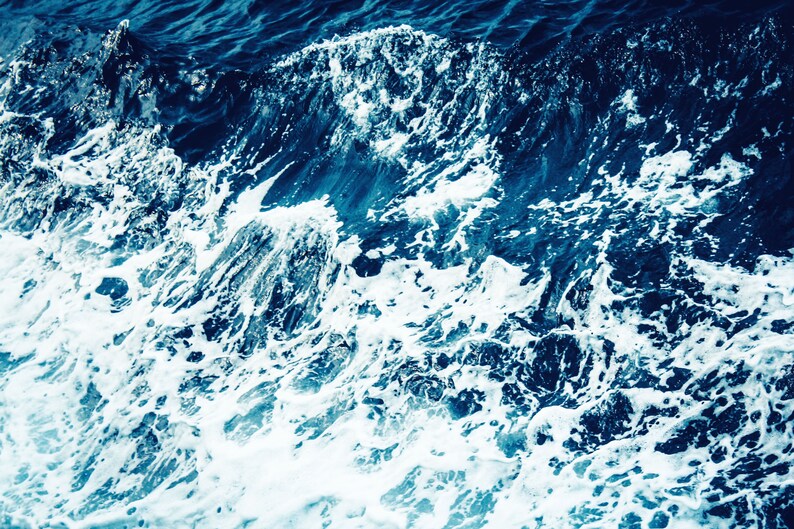 May include: Close-up of white foam waves crashing on a deep blue ocean surface.