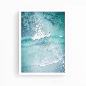 May include: An aerial view of turquoise ocean water with white foamy waves and several surfers in the water.
