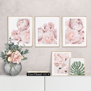 Op de afbeelding: Vier ingelijste prints van roze pioenrozen met gouden lijsten, een boek getiteld "Coco Chanel" en een vaas met roze bloemen op een wit oppervlak.