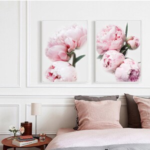 May include: Two framed prints of pink peonies with white backgrounds. The prints are hung on a white wall above a bed with pink bedding.