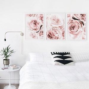 May include: Three framed prints of pink roses, arranged in a row on a white wall above a white bed with a black and white patterned pillow.