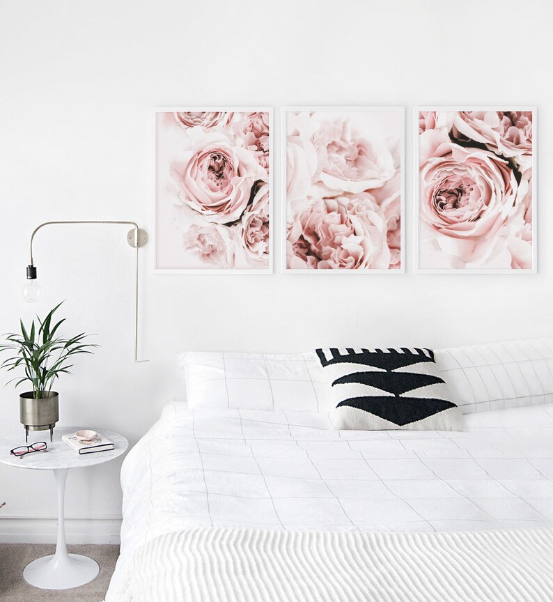 May include: Three framed prints of pink roses, arranged in a row on a white wall above a white bed with a black and white patterned pillow.