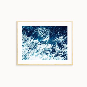 May include: A close-up photograph of a blue ocean with white foamy waves crashing.