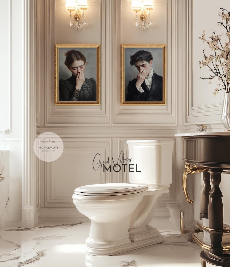 May include: A white toilet with a white tank and a gold trim. The toilet is in a bathroom with white walls and a brown wooden vanity with gold accents. There are two framed paintings on the wall, one of a woman and one of a man. The text "Good Vibes Motel" is written on the wall above the toilet.