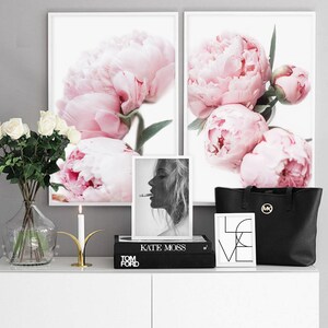 May include: Two framed prints of pink peonies, a black and white photo of Kate Moss, a black tote bag with a gold logo, a gold candle holder with a white candle, and a black book with the text "TOM FORD" and "KATE MOSS" on the spine.