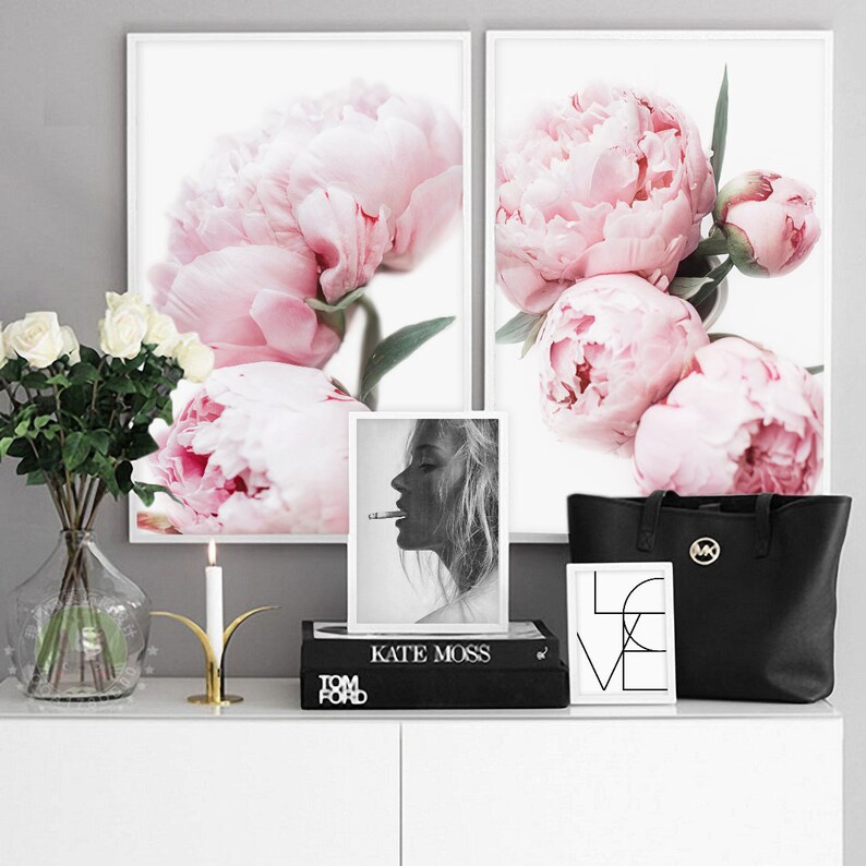 May include: Two framed prints of pink peonies, a black and white photo of Kate Moss, a black tote bag with a gold logo, a gold candle holder with a white candle, and a black book with the text "TOM FORD" and "KATE MOSS" on the spine.