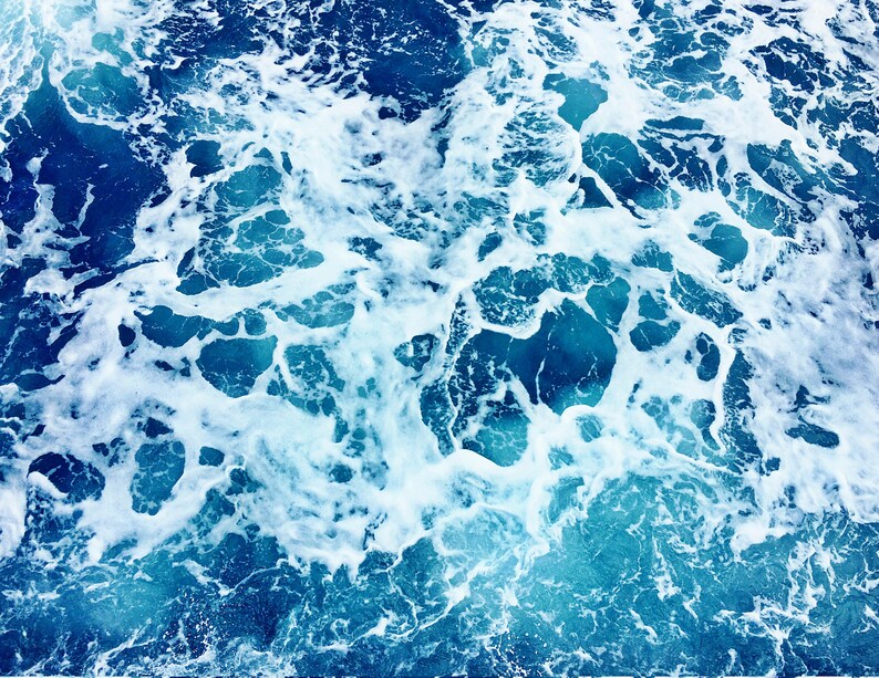 May include: A close-up of white foam on top of a deep blue ocean. The foam is in a swirling pattern, creating a textured look.