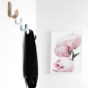 May include: A white wall with a set of wooden and blue hooks, a black jacket hanging on the hooks, and a framed print of pink peonies.