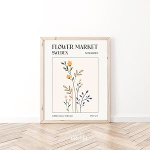 May include: A framed poster with a minimalist design featuring a floral illustration in shades of pink, yellow, and blue. The poster has the text "FLOWER MARKET SWEDEN STOCKHOLM" and "Exhibition Flower Collection 1998 No.9".