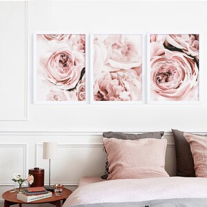 May include: Three framed prints of close-up photos of pink roses. The prints are arranged in a row on a white wall above a bed with pink and gray bedding.