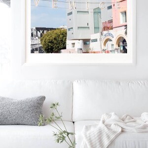 May include: A framed photograph of a street scene in Venice, California. The photo features a bright blue sky, a white building with a green tree in front of it, and a sign that reads "Venice Beach Market".
