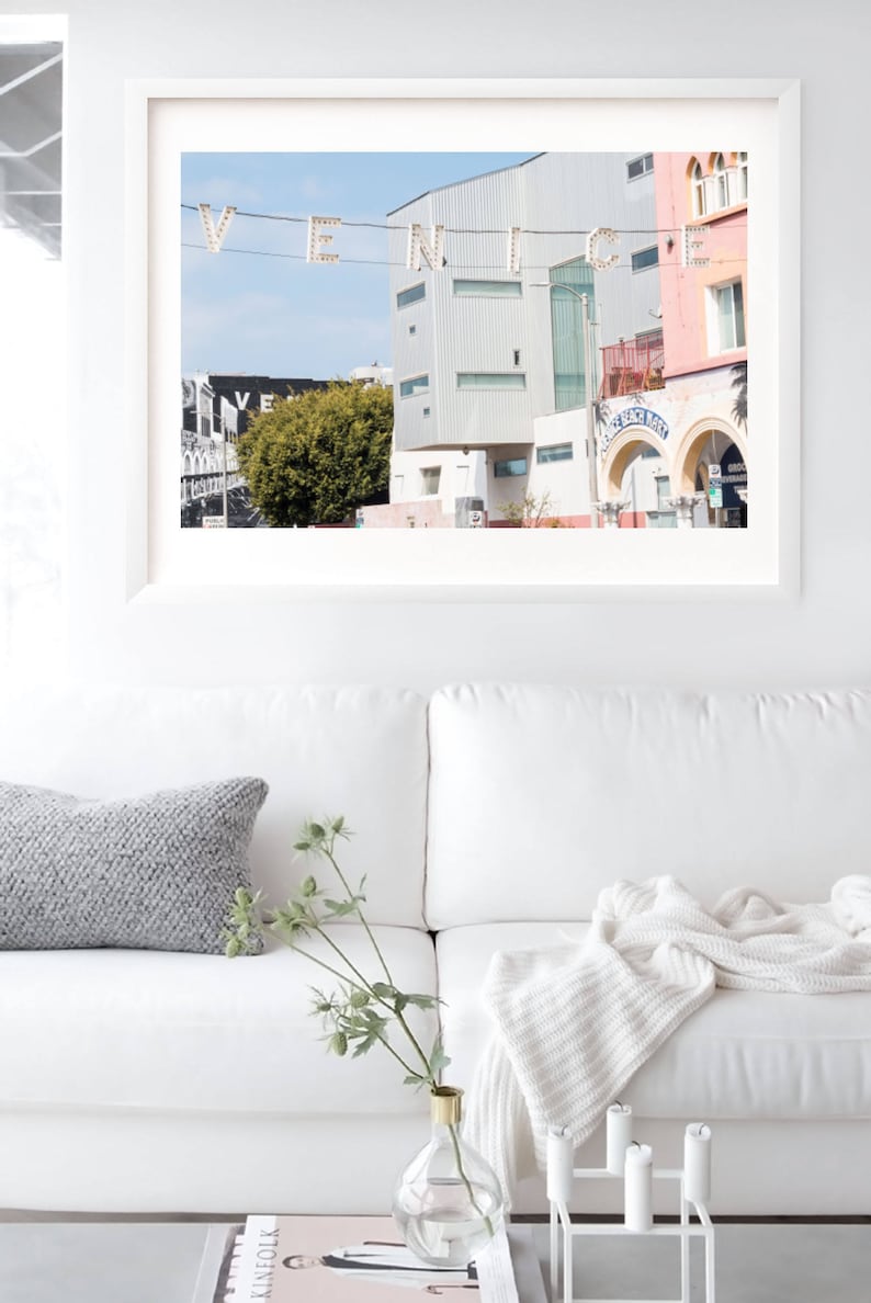 May include: A framed photograph of a street scene in Venice, California. The photo features a bright blue sky, a white building with a green tree in front of it, and a sign that reads "Venice Beach Market".