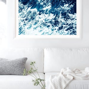 May include: A close-up photograph of a blue ocean with white foamy waves crashing. The image is taken from above the water, looking down at the waves.