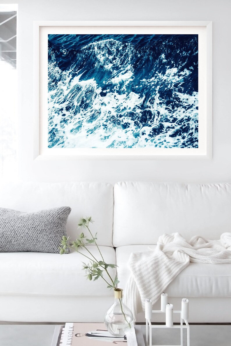 May include: A close-up photograph of a blue ocean with white foamy waves crashing. The image is taken from above the water, looking down at the waves.