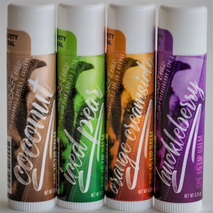 May include: Four lip balm tubes with different flavors: Coconut, Iced Pear, Orange Creamsicle, and Huckleberry. Each tube has a white cap and a colorful label with the flavor name and a graphic design. The lip balms are SPF 15.
