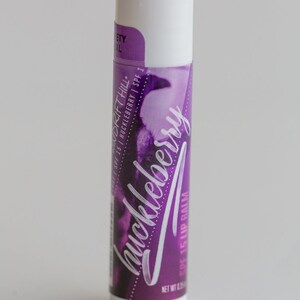 May include: A white tube of huckleberry flavored lip balm with a purple and white label. The label says "Drift Hill" and "SPF 15 Huckleberry SPF 1".
