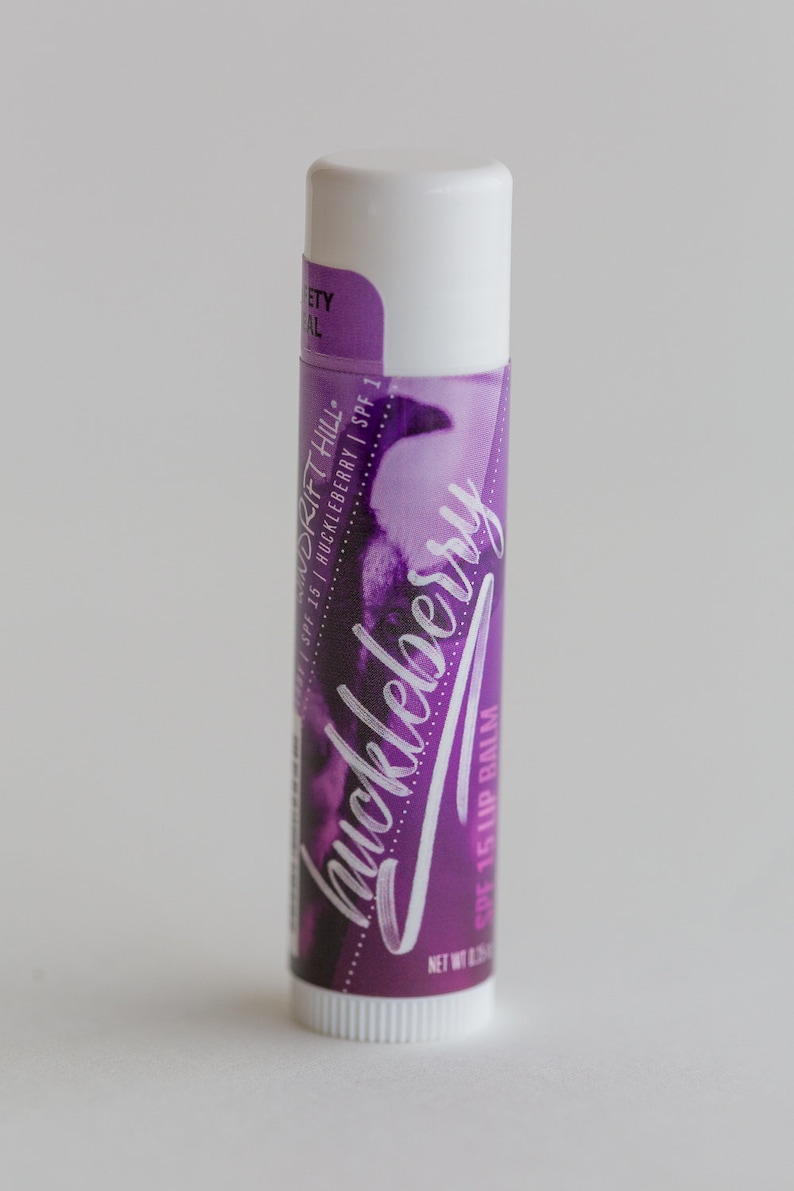 May include: A white tube of huckleberry flavored lip balm with a purple and white label. The label says "Drift Hill" and "SPF 15 Huckleberry SPF 1".