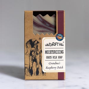 May include: A brown cardboard box with a red stripe on the side. The box contains a bar of goat milk soap with a raspberry scent. The box has a picture of a goat and the text "Windrift Hill Moisturizing Goats Milk Soap Grandma's Raspberry Patch".