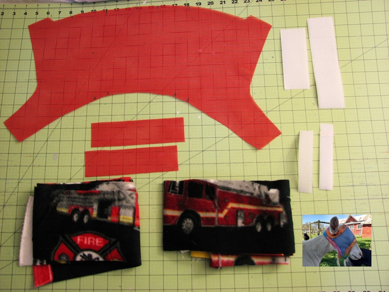 Puede incluir: Un patr&oacute;n de tela roja con dos tiras de tela roja y cuatro tiras de tela blanca. Hay dos piezas de tela con un estampado de cami&oacute;n de bomberos y logotipo del departamento de bomberos. Una pieza de tela est&aacute; doblada y la otra est&aacute; enrollada. Hay una foto de un caballo con una m&aacute;scara de tela roja y negra.