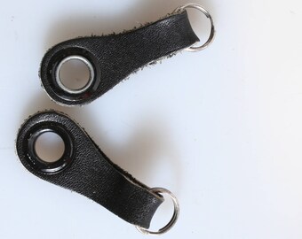 May include: Two black leather key fobs with silver metal rings. Each fob has a round metal eyelet.