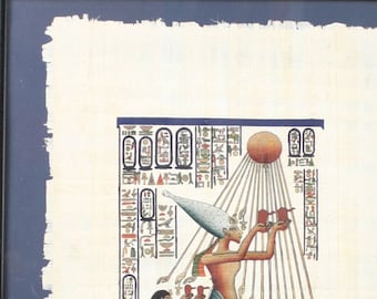 May include: A framed papyrus print depicting an Egyptian goddess with a white headdress, holding a cup and standing with two other figures. The print is surrounded by hieroglyphs and a sun symbol.