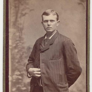 Puede incluir: Un retrato en blanco y negro de un hombre con una chaqueta a rayas. La foto está enmarcada con un borde dorado y rojo. El texto "WILLIAMS, 210 LOCUST ST. COLUMBIA, PA." está impreso en la parte inferior de la foto.
