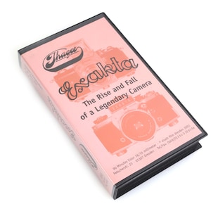 May include: A pink box with the text "Exakta: The Rise and Fall of a Legendary Camera" and a camera illustration. The box has a black border and the Thagee logo.