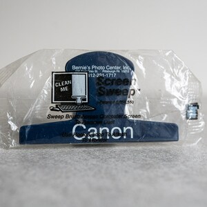 May include: A blue plastic screen cleaning tool with a small brush and a hook to attach to a monitor. The tool is packaged in a clear plastic bag and has the text "Screen Sweep" and "Canon" printed on it.