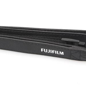 May include: Black camera strap with the white "FUJIFILM" logo. The strap is made of a textured material and features a black plastic buckle. The strap is designed to be worn around the neck or shoulder.