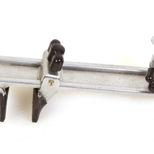 Op de afbeelding: Een zilveren metalen cameraschuif met twee zwarte rubberen klemmen en een zwarte kogelkop met een knop bovenop.