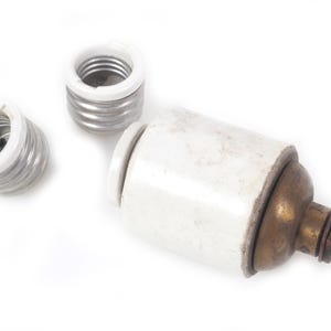 May include: A vintage electrical light socket component featuring a cylindrical white ceramic housing, a tarnished brass base with a pull-chain mechanism, and two separate threaded metal light bulb socket inserts with white ceramic rims.