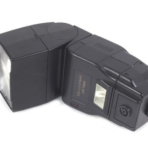 May include: A black camera flash unit with a rectangular head and a pivoting body. The flash has a built-in light and a control panel with the text "OLIVIAKA" and "CF-5000A". The unit is designed for professional photography.