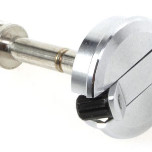 Puede incluir: Una herramienta mecánica plateada y negra. Presenta un cuerpo cilíndrico, una cabeza ranurada y un eje plateado. También hay un componente negro en forma de engranaje. La herramienta está diseñada para una función mecánica específica.