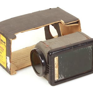 May include: Vintage Brownie Safelight Lamp Model C with its original cardboard box. The lamp is black and gray with a lens and a threaded fitting. The box is brown with yellow text.