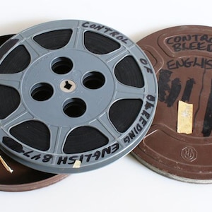 May include: A vintage film reel with the text "CONTROL OF BLEEDING ENGLISH" in black lettering. The reel is gray and sits inside a brown metal case. The case lid is also visible, with similar text.