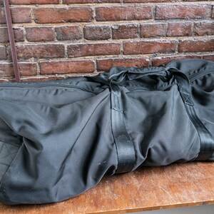 Könnte beinhalten: Eine schwarze Reisetasche mit Reißverschluss und zwei schwarzen Riemen.
