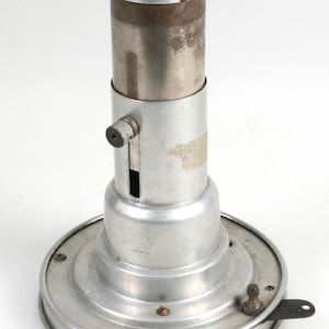 May include: A silver metal magnifying lamp with a round base and a cylindrical magnifying glass. The lamp has a switch on the side and a small knob on the side of the magnifying glass.